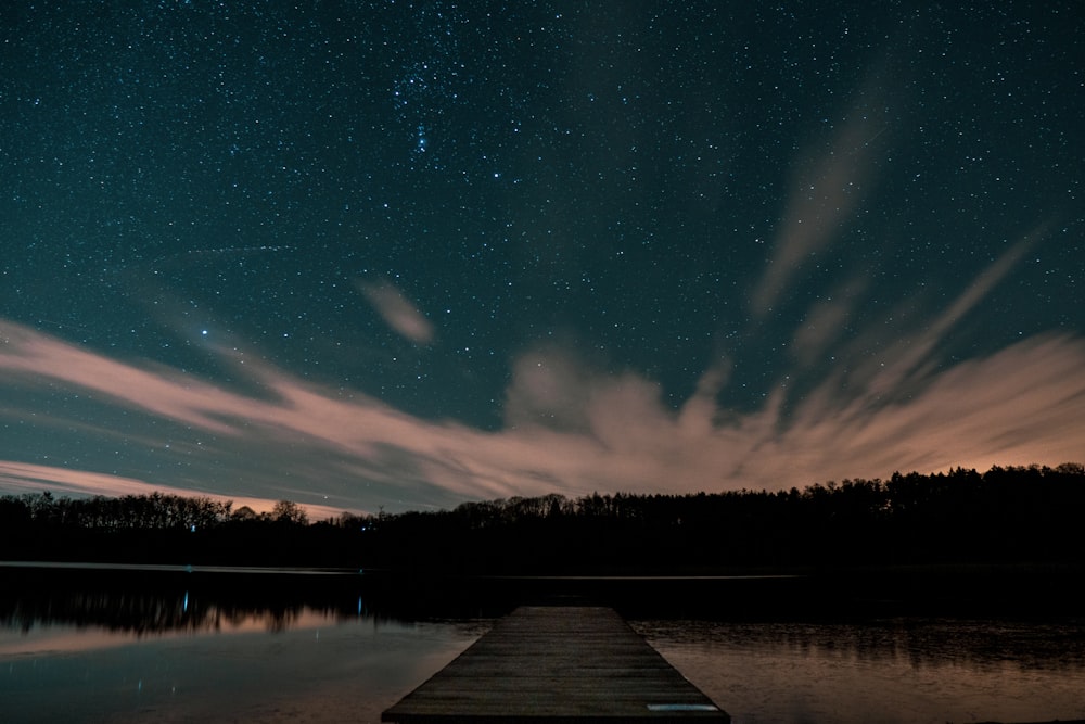 a wooden dock sitting on top of a lake under a night sky