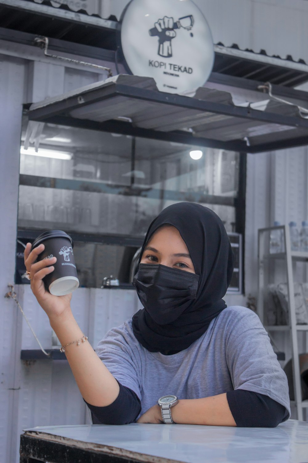 a woman wearing a face mask holding a cup of coffee