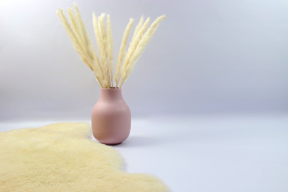 a pink vase with some dry grass in it