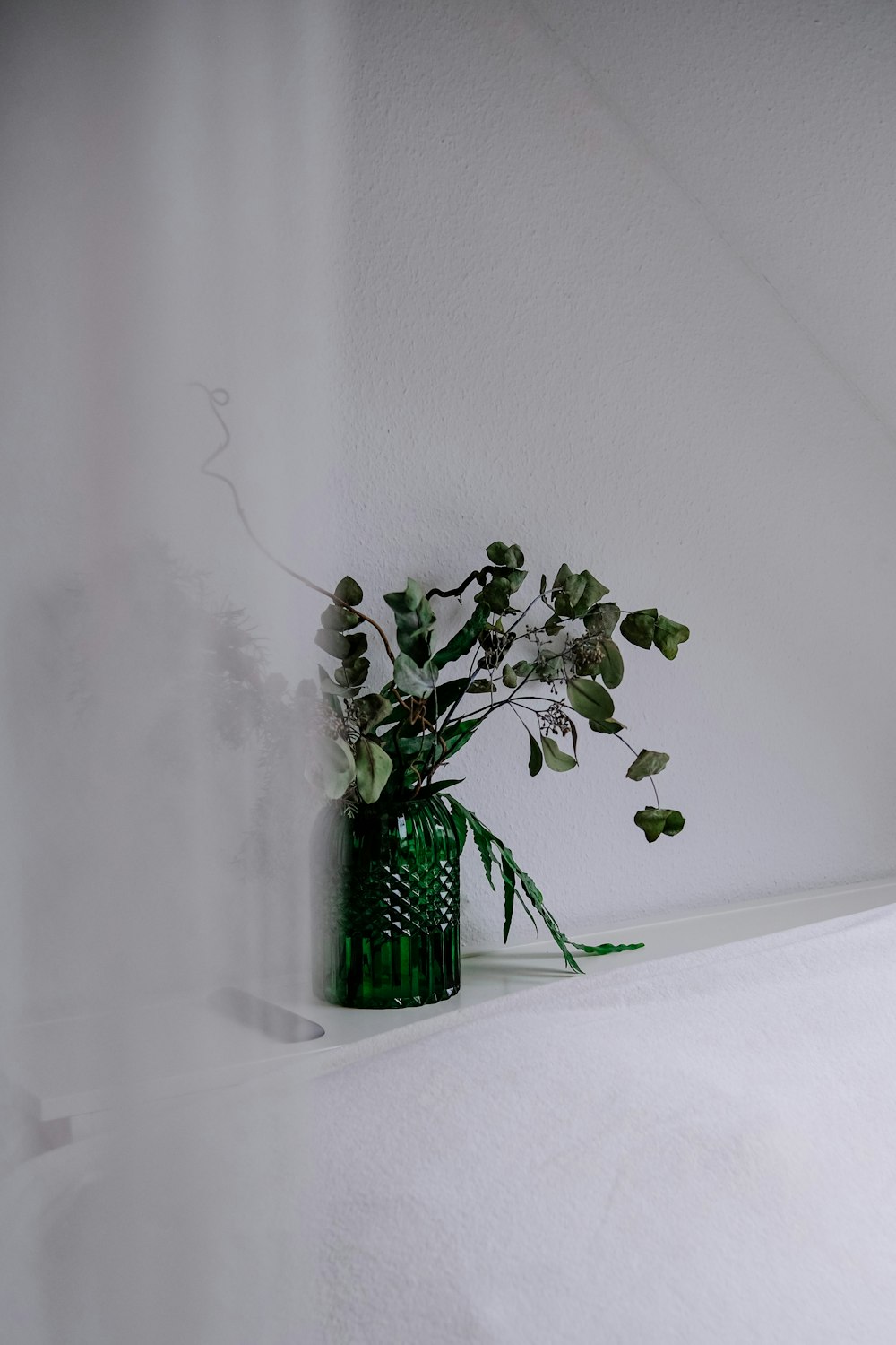 a green vase filled with flowers on top of a shelf