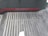 A set of wide, concrete stairs with a red handrail on the left side. The steps are equipped with white tactile paving dots, likely for aiding visually impaired individuals. The floor and the surrounding walls are made of dark materials. A white rectangular object appears at the bottom center of the stairs.