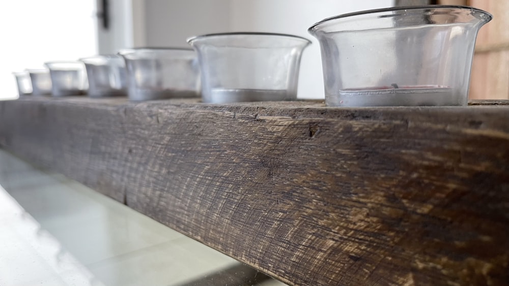 a row of glass cups sitting on top of a wooden shelf