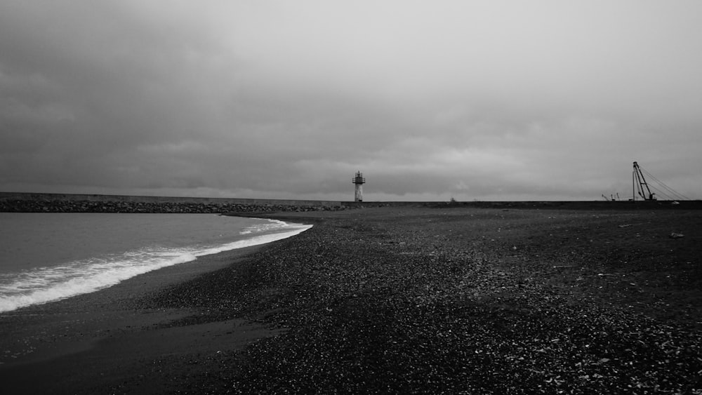 a black and white photo of a beach and lighthouse