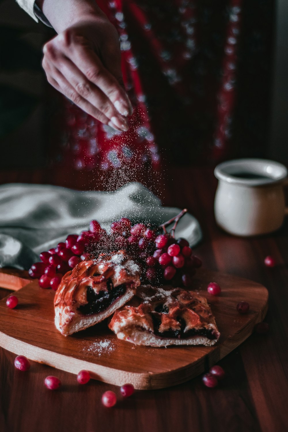 a person sprinkling cranberries on top of a wooden cutting board