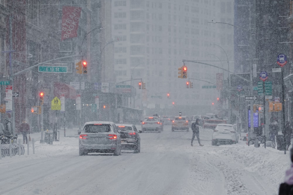 a couple of cars driving down a snow covered street