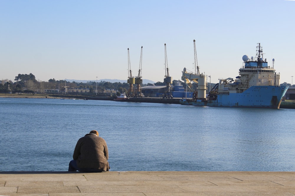a man sitting on the edge of a pier next to a body of water