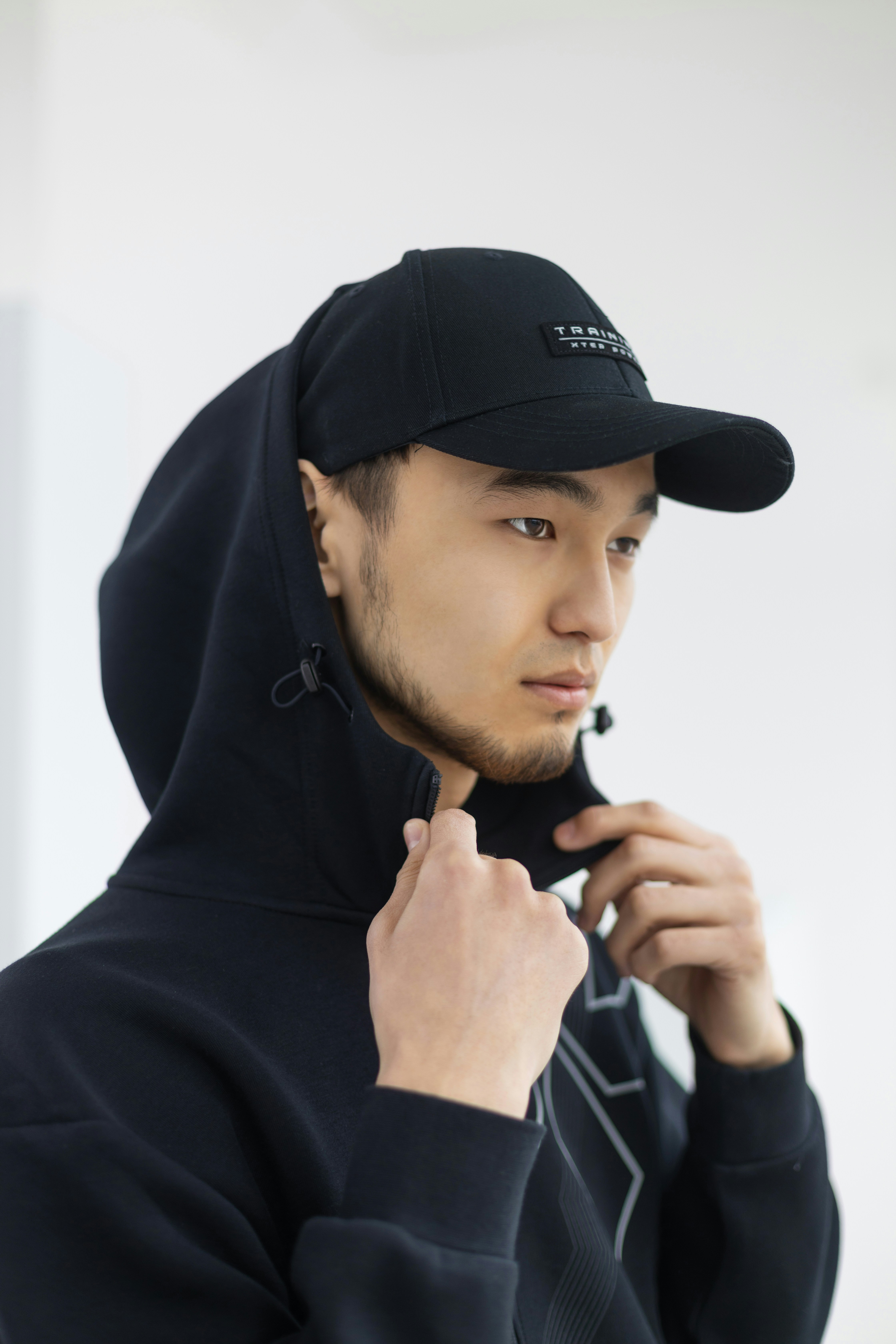 a man in a black hoodie adjusting his cap