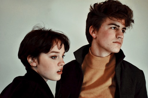 A young man and woman examining their skin in a bright, cozy room, both looking thoughtful and hopeful.