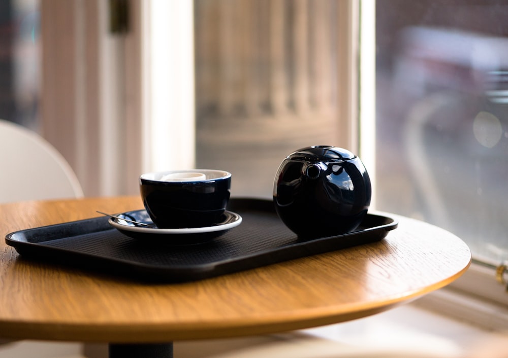 a wooden table topped with a black tea cup and saucer