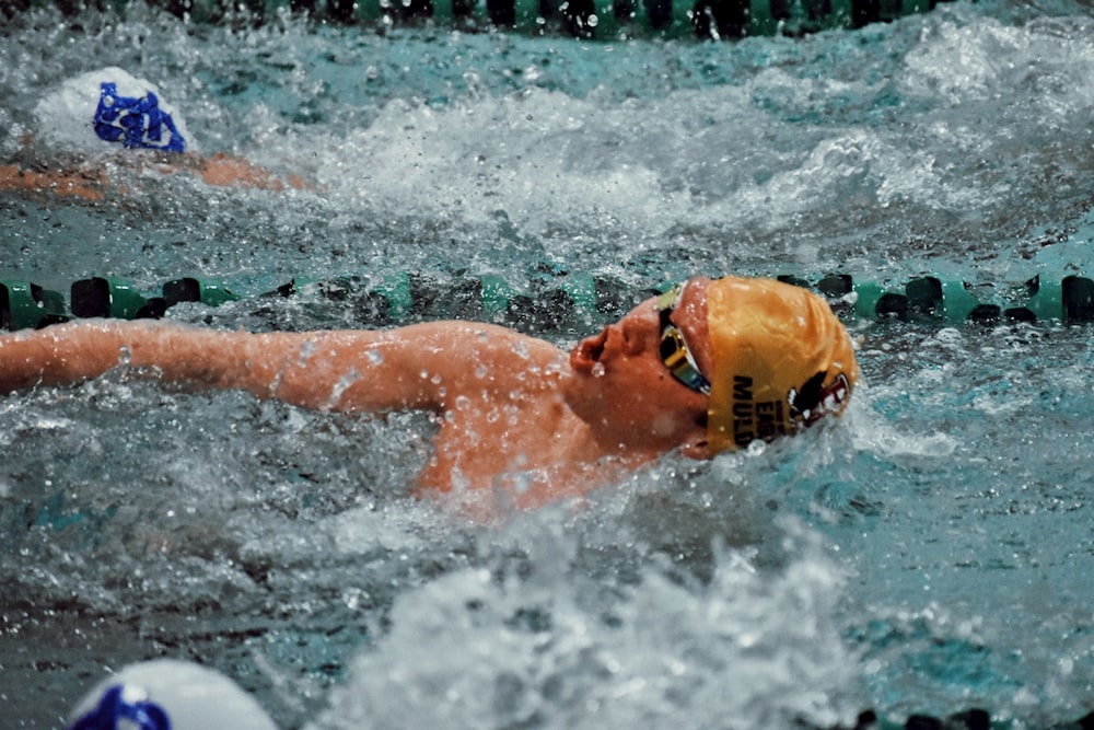 Un hombre nadando en una piscina con un sombrero amarillo