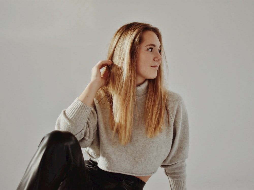 a woman sitting on the floor wearing a sweater and black pants