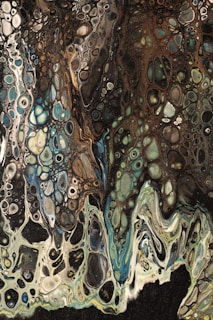 An abstract fluid art piece with intricate patterns and a marbled effect. Shades of green, blue, brown, and black blend together, creating a sense of movement and depth. Organic shapes and circular formations give the impression of a natural, organic texture.