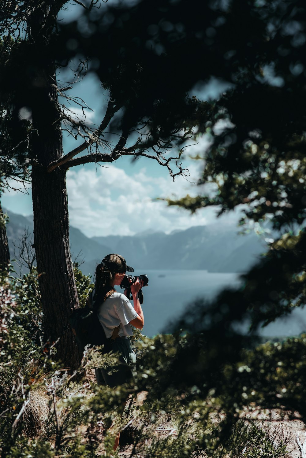 a woman taking a picture of a lake through the trees