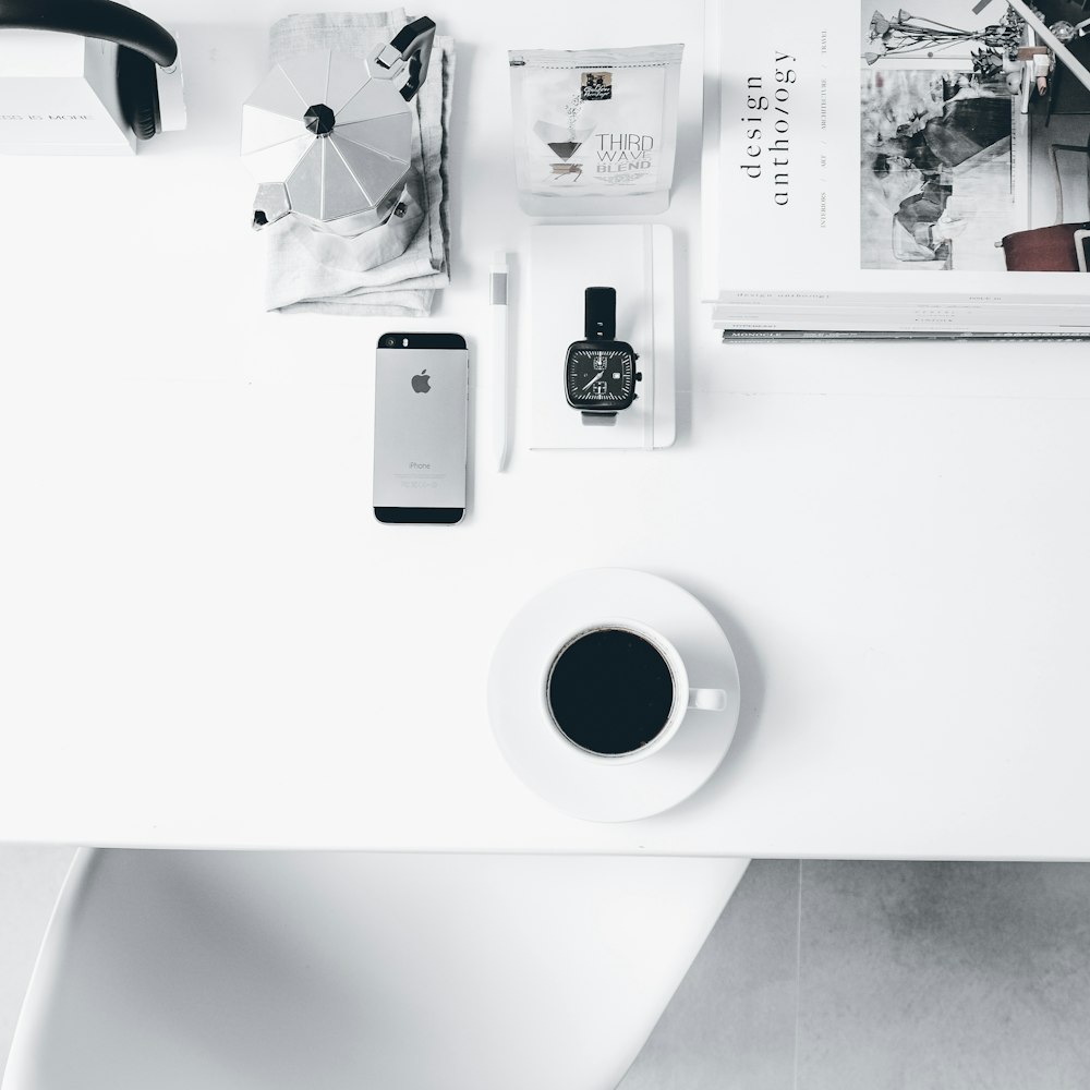 un bureau blanc avec une tasse de café et un téléphone portable