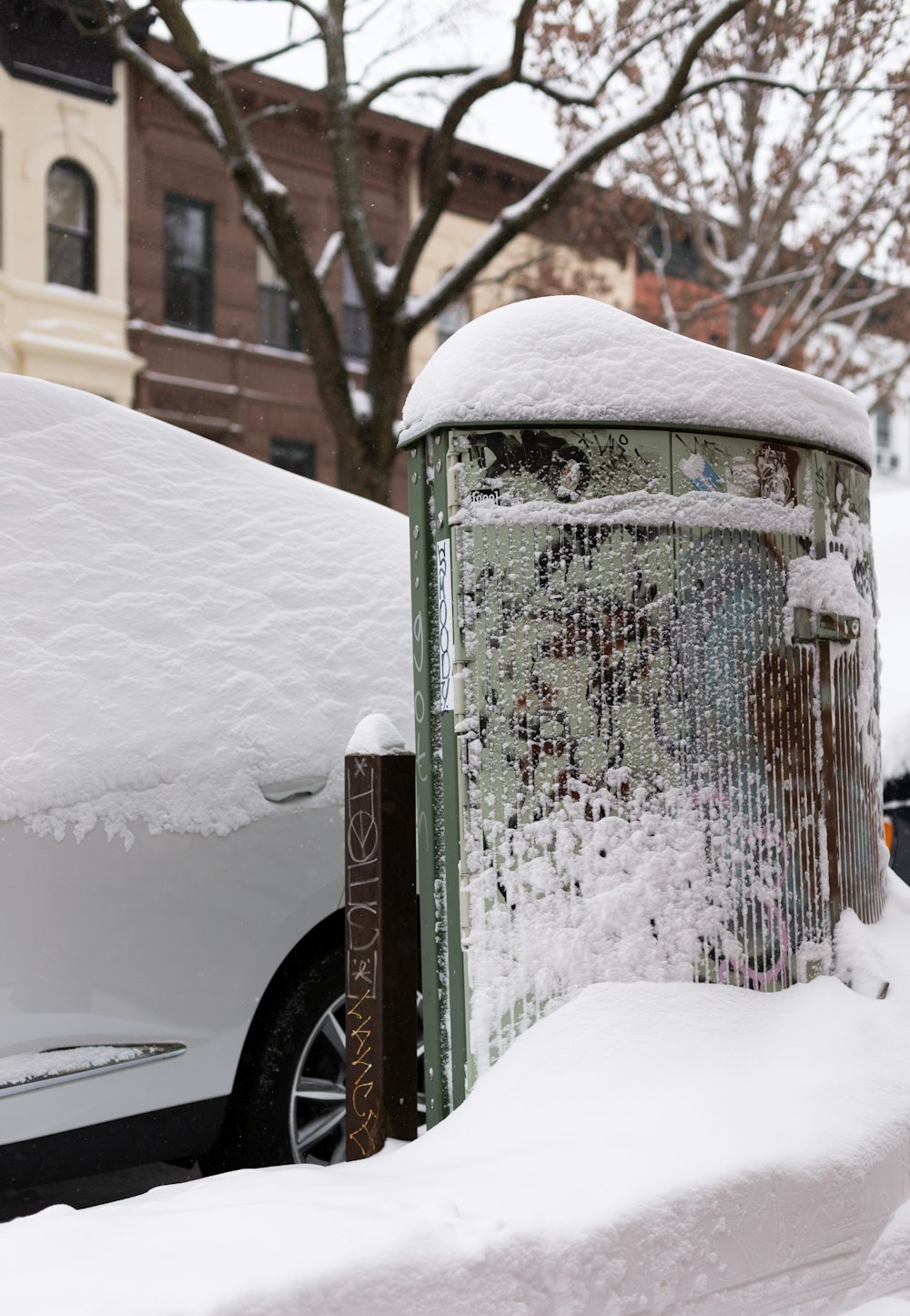 a parking meter covered in snow next to a white car