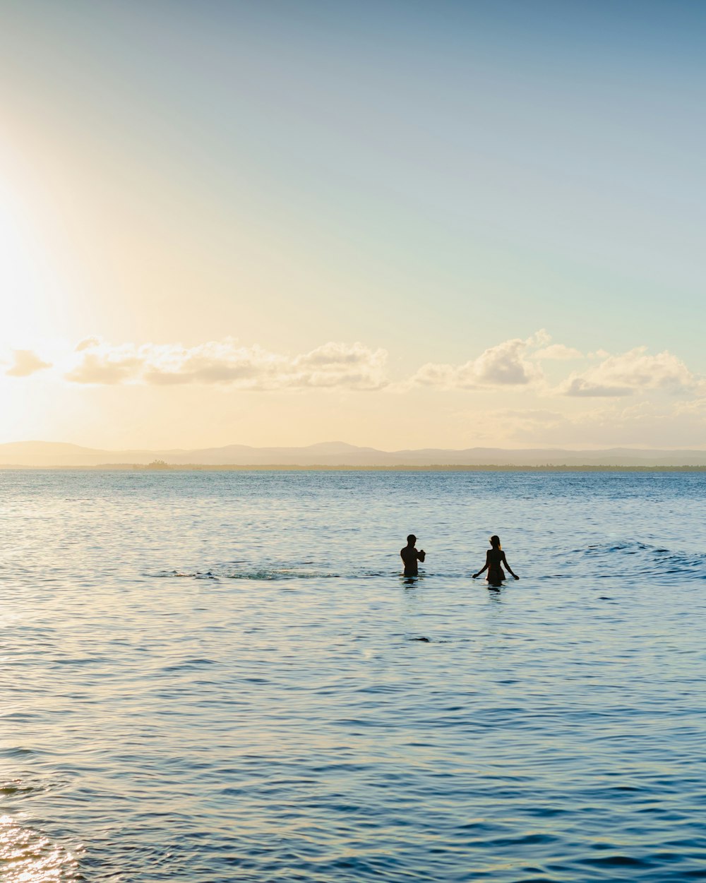 two people are wading in the ocean at sunset