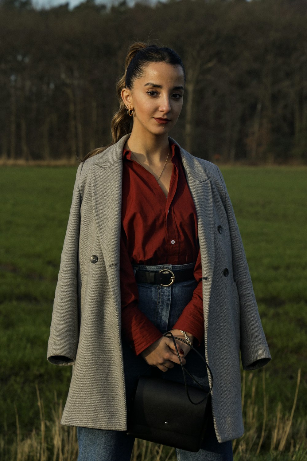 a woman standing in a field holding a black purse