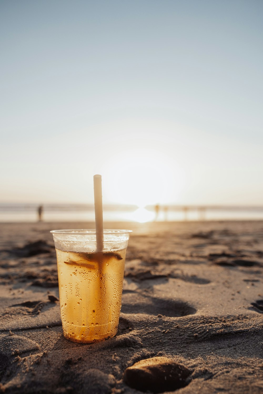 a plastic cup with a straw on a beach