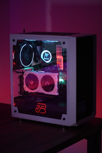 A gaming computer with visible internal components such as cooling fans and LED lights in a transparent case. The lighting emits a colorful glow with shades of purple, blue, and red.