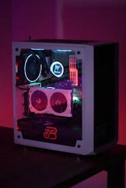A gaming computer with visible internal components such as cooling fans and LED lights in a transparent case. The lighting emits a colorful glow with shades of purple, blue, and red.