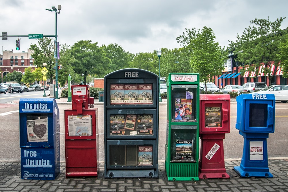 a row of newspaper dispensers sitting on the side of a road