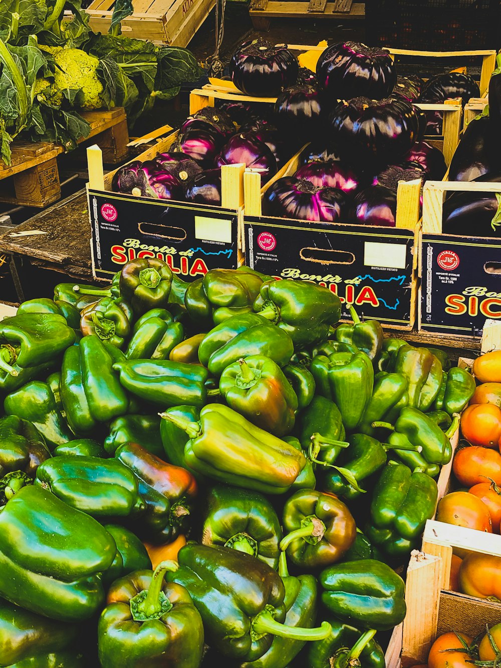 a pile of green peppers sitting next to boxes of tomatoes