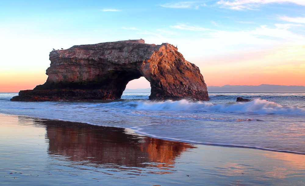 a large rock sticking out of the ocean next to a beach