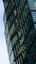 A modern building with a geometric facade featuring numerous green-tinted glass windows and black structural elements, creating an intricate pattern.