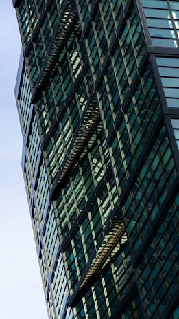 A modern building with a geometric facade featuring numerous green-tinted glass windows and black structural elements, creating an intricate pattern.
