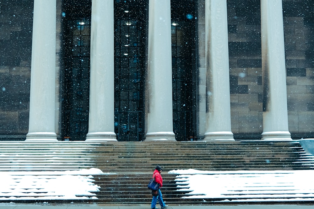 two people walking in the snow in front of a building