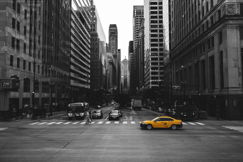 a yellow car driving down a street next to tall buildings