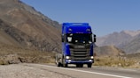a blue semi truck driving down a mountain road