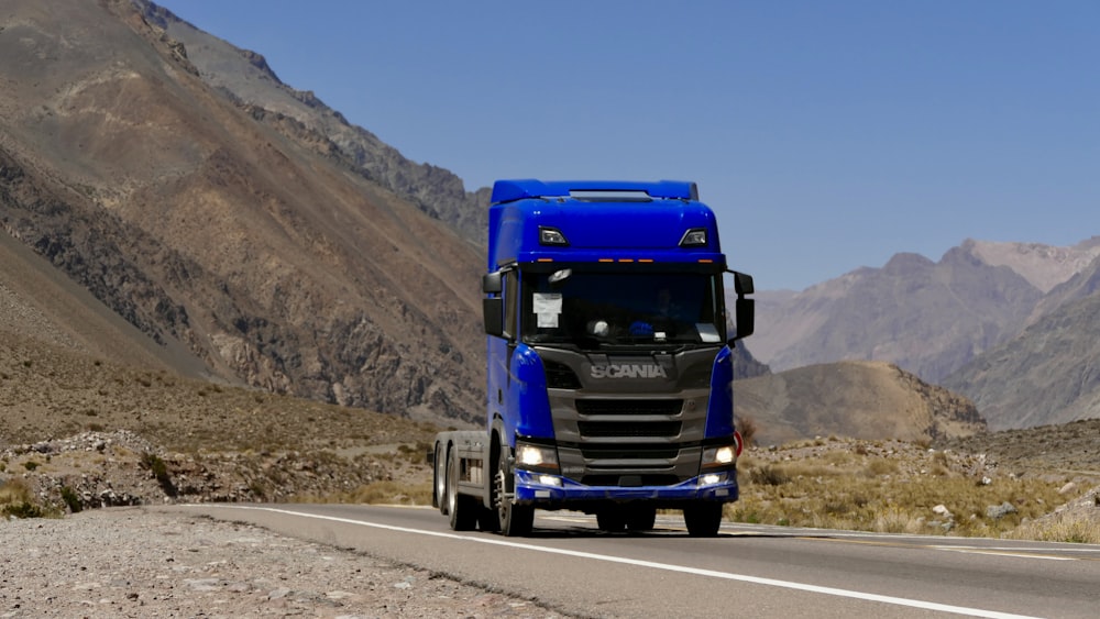 a blue semi truck driving down a mountain road