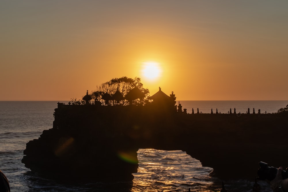 the sun is setting over the ocean with a rock formation in the foreground