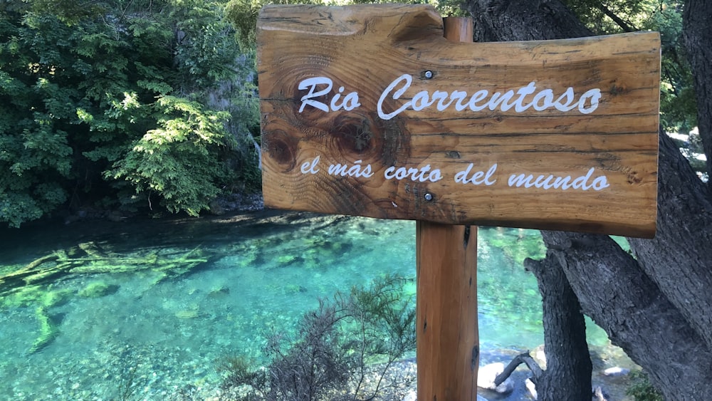 a wooden sign sitting on the side of a river
