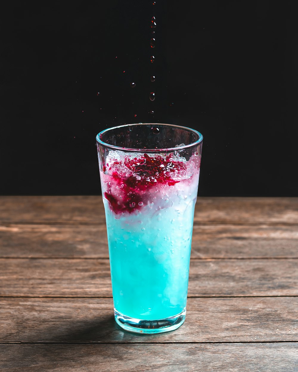 a glass filled with blue liquid on top of a wooden table