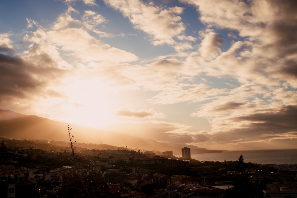 the sun is setting over a city with mountains in the background