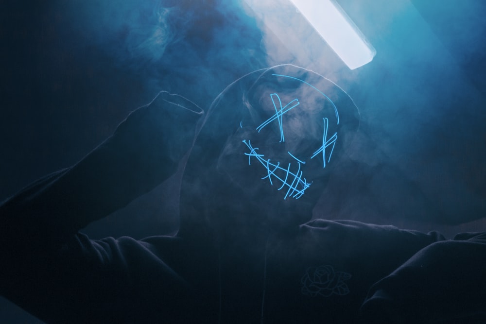 a person in a dark room with a neon mask