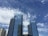 Tall skyscrapers with reflective glass windows rise against a backdrop of a clear blue sky with scattered clouds. The buildings feature modern architecture, with the sign 'Bruno Central Plaza' visible on one of them.