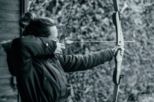 a woman holding a bow and aiming it at a target