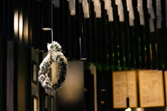 A decorative wreath is suspended from the ceiling, illuminated by soft lighting. The background features a modern interior with dark tones and a blurred view of what appears to be menu boards on a wall.