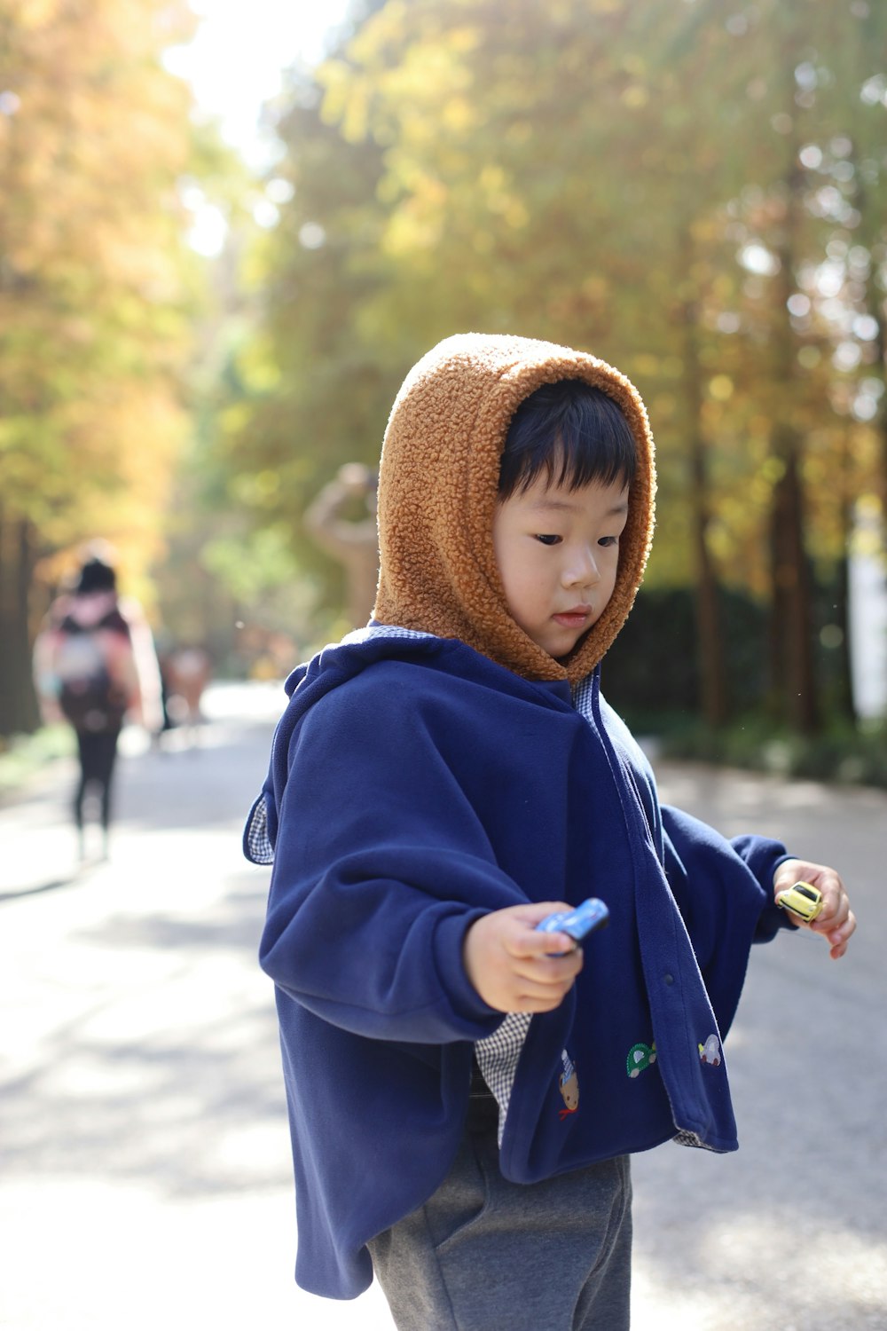 Ein kleiner Junge in einem blauen Kapuzenpulli, der ein Handy hält