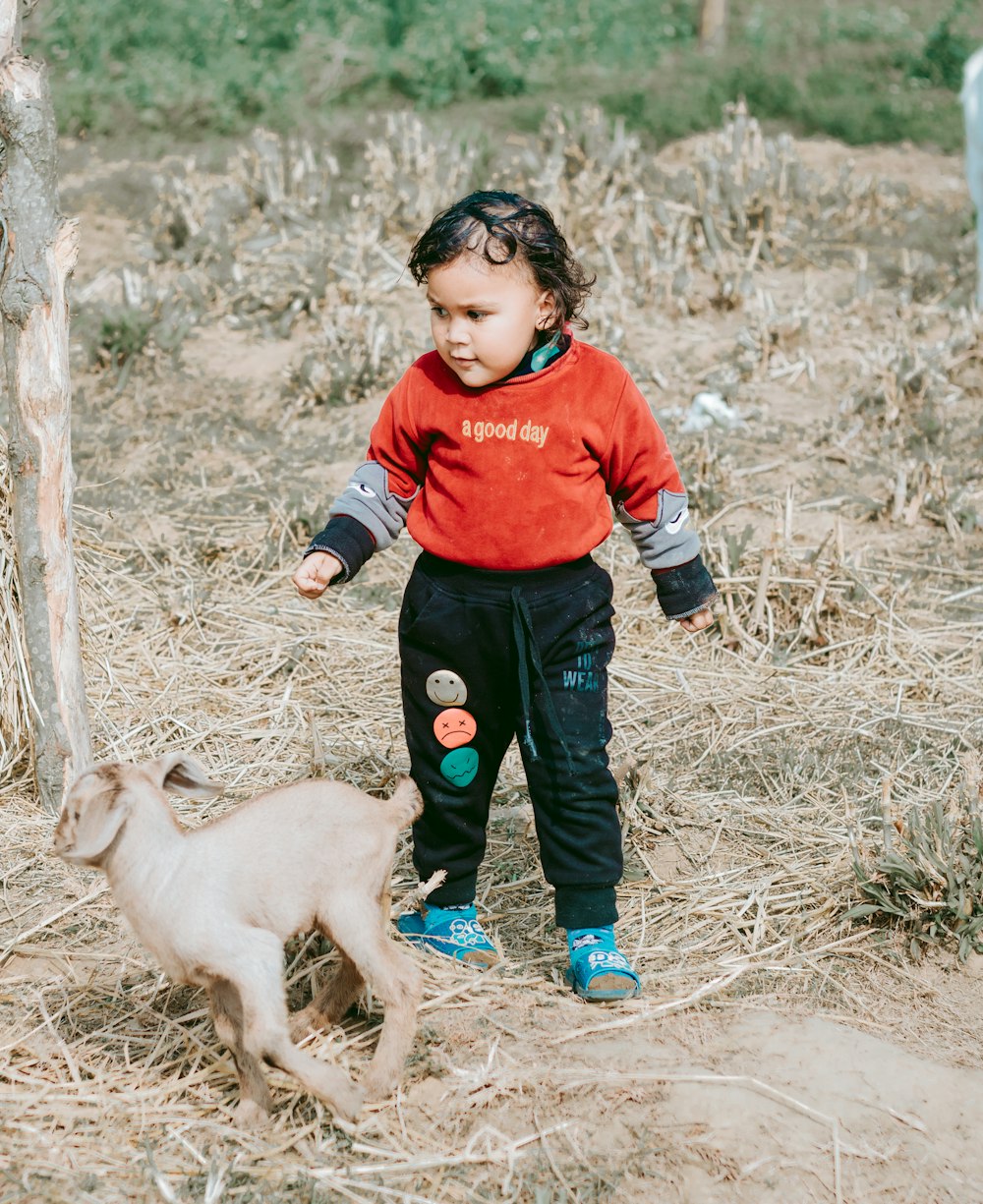 Un niño pequeño parado junto a una cabra bebé