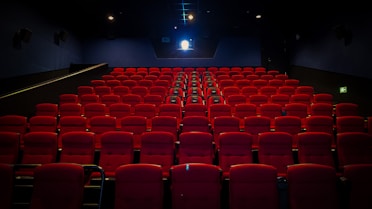 an empty theater with red seats and a projector screen