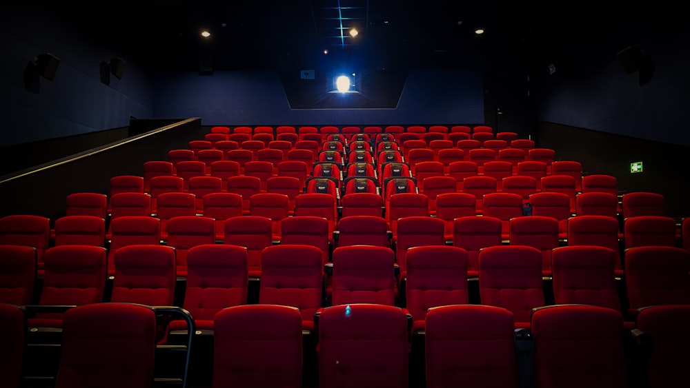 an empty theater with red seats and a projector screen