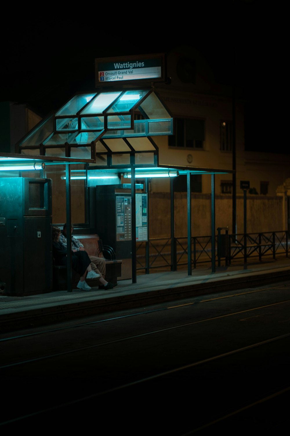 a train station at night with a person sitting on a bench