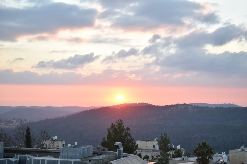 the sun is setting over a city with mountains in the background