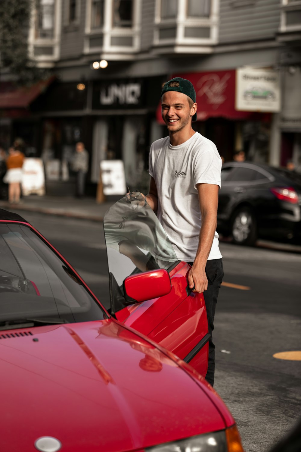 a man standing next to a red car on a city street