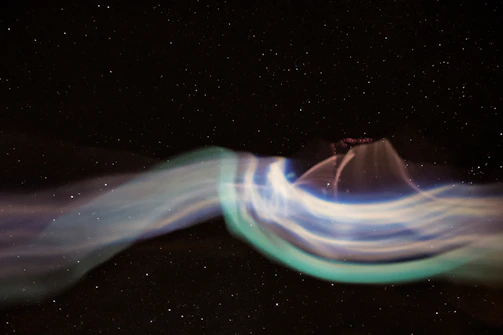 Soft cosmic waves of blue and white light flowing across a midnight sky with twinkling stars.