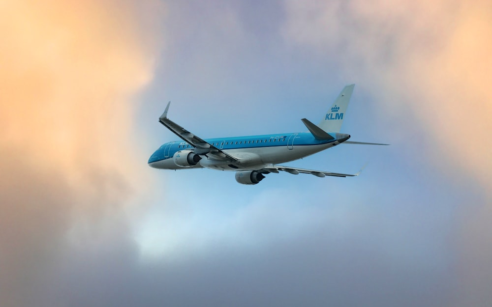 a blue and white airplane flying through a cloudy sky